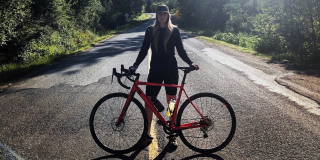 Alexandra Vallée stands with her bike on a winding road.