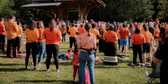 A group of people stand in a park wearing their orange shirts for Orange Shirt Day.