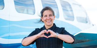 Teara Fraser smiles in front of a plane. She's making a heart shape with her hands.