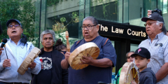 A group of Indigenous folks stand with drums outside the Law Courts.