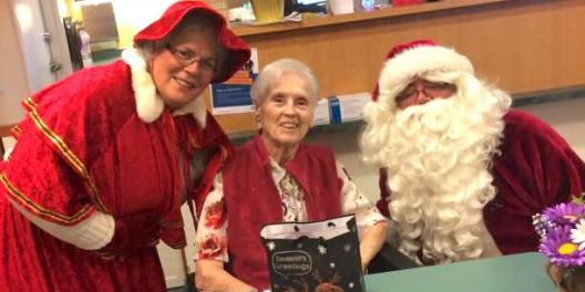 Folks dressed as Santa and Mrs Claus pose for a photo with a local senior.