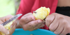 A closeup of hands peeling potatoes.